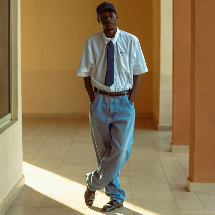 Un uomo sta in piedi con le gambe incrociate e indossa una camicia bianca, una cravatta e pantaloni larghi.