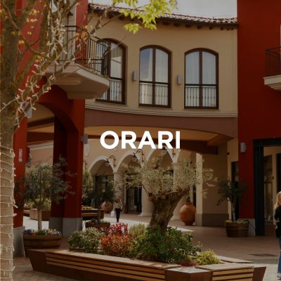 L'immagine mostra una parte del centro commerciale, un passaggio e, sullo sfondo, i negozi fiancheggiati da archi a tutto sesto. L'immagine riporta inoltre il titolo: Orari di apertura