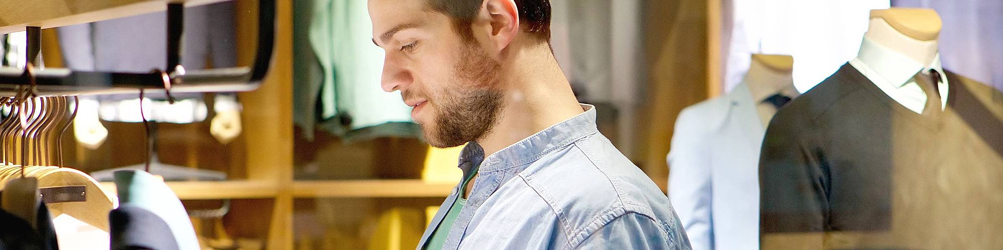 Si vede un uomo in piedi in un negozio, dietro di lui due manichini.