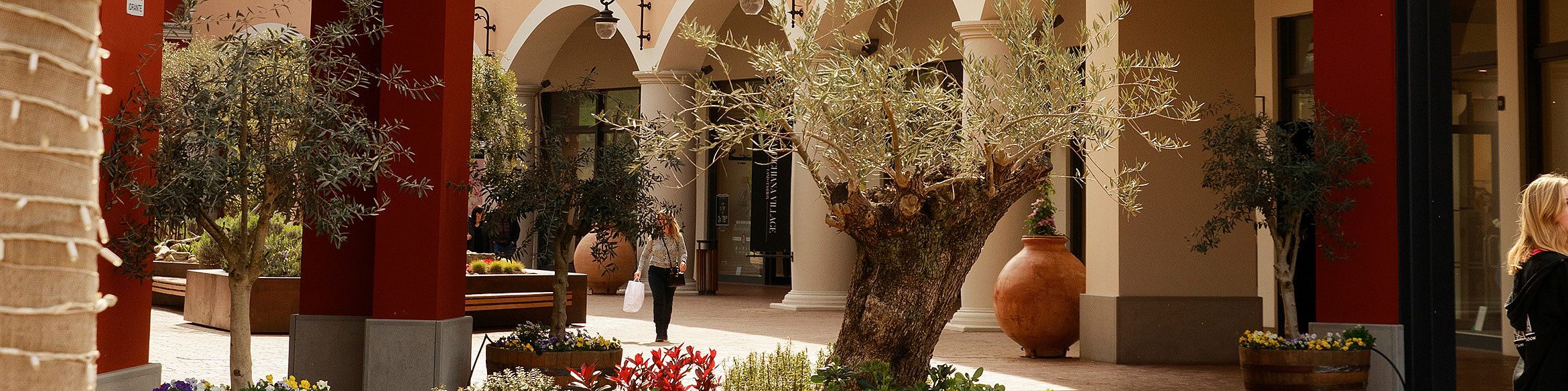 L'immagine mostra una parte del centro commerciale, un passaggio e, sullo sfondo, i negozi fiancheggiati da archi a tutto sesto.